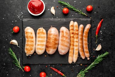 Baharatlı ızgara sosisler ve siyah arka planda otlar. 