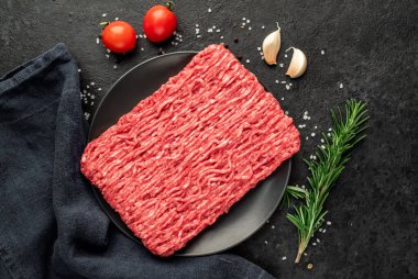 Baharatlı çiğ et ve siyah arka planda otlar.