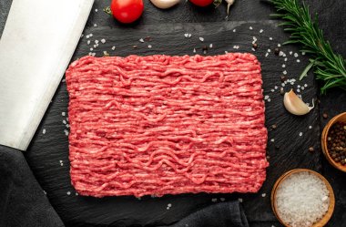 Baharatlı çiğ et ve siyah arka planda otlar.