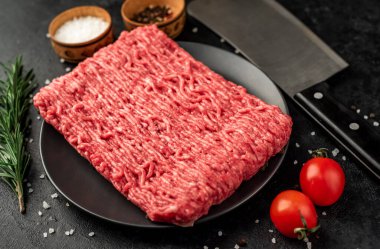 Baharatlı çiğ et ve siyah arka planda otlar.