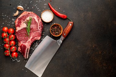 Baharatlı çiğ biftek ve siyah arka planda otlar.