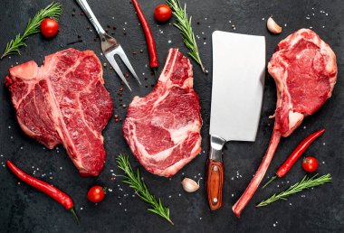 Biberiyeli çiğ biftek ve siyah arka planda baharatlar.