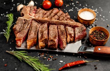 Baharatlı ızgara biftek ve siyah arka planda otlar.