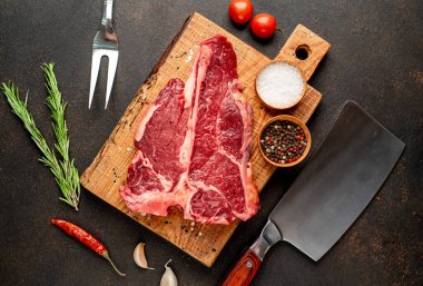 Baharatlı çiğ biftek ve siyah arka planda otlar.