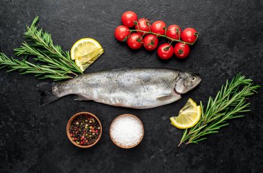 Baharatlı çiğ dorado balığı ve siyah arka planda otlar.