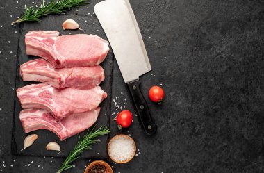 Baharatlı çiğ domuz pirzolası ve siyah arka planda otlar. 