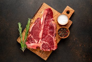 Baharatlı çiğ biftek ve siyah arka planda otlar.