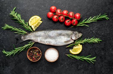 Baharatlı çiğ dorado balığı ve siyah arka planda otlar.