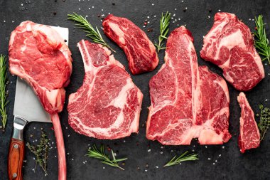 Baharatlı çiğ biftek ve siyah arka planda otlar.