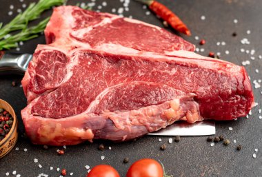 Baharatlı çiğ biftek ve siyah arka planda otlar.