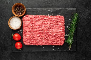 Baharatlı çiğ et ve siyah arka planda otlar.