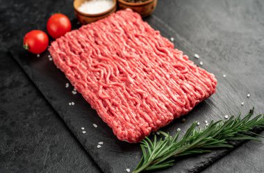 Baharatlı çiğ et ve siyah arka planda otlar.