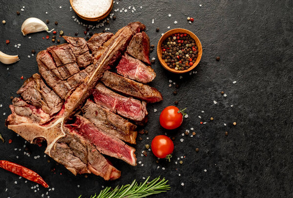 grilled beef steak with spices and herbs on black background