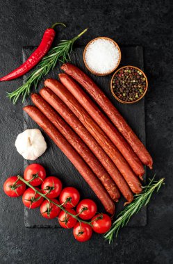 Biberiyeli çiğ sosisler ve siyah arka planda bitkiler.