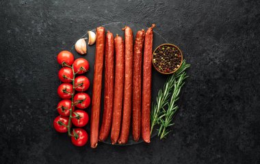 Baharatlı çiğ sosisler ve siyah arka planda bitkiler. Üst Manzara. Metnin için boş yer.