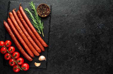 Baharatlı çiğ sosisler ve siyah arka planda bitkiler.