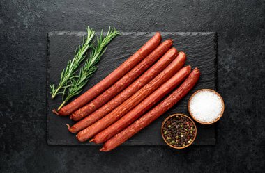 Biberiyeli çiğ sosis ve siyah arka planda baharatlar.