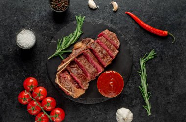 Baharatlı ızgara biftek ve siyah arka planda otlar.