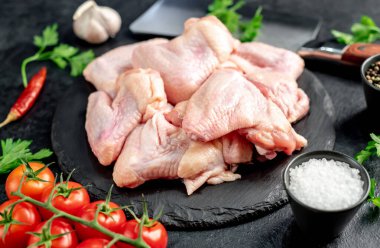 Siyah arka planda baharatlı ve otlu çiğ tavuk kanatları.