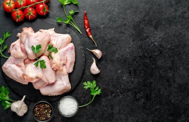 Siyah arka planda baharatlı ve otlu çiğ tavuk kanatları.