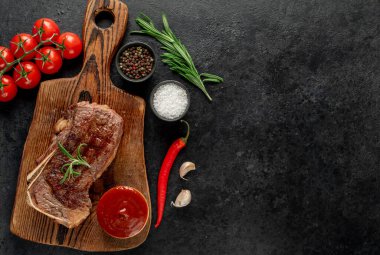 Baharatlı ızgara biftek ve siyah arka planda otlar.