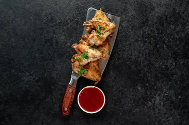 Baharatlı kızarmış tavuk kanatları ve siyah arka planda otlar.