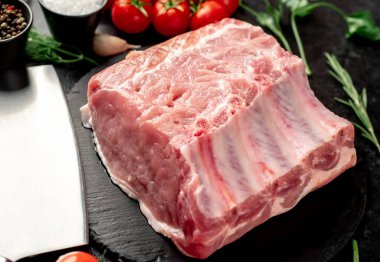 Baharatlı çiğ biftek ve siyah arka planda otlar.