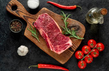 Baharatlı çiğ biftek ve siyah arka planda otlar.