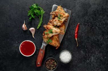 Baharatlı kızarmış tavuk kanatları ve siyah arka planda otlar.