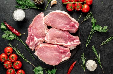 Baharatlı çiğ biftek ve siyah arka planda otlar.