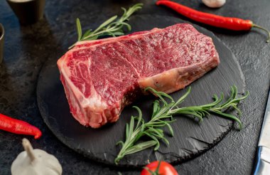 Baharatlı çiğ biftek ve siyah arka planda otlar.