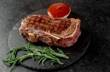 Baharatlı ızgara biftek ve siyah arka planda otlar.