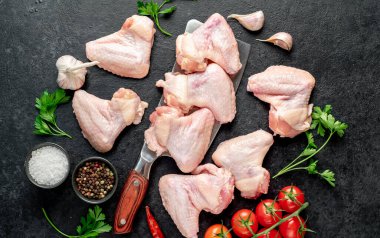 Siyah arka planda baharatlı ve otlu çiğ tavuk kanatları.