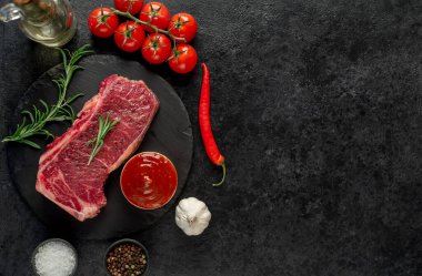 Baharatlı çiğ biftek ve siyah arka planda otlar.