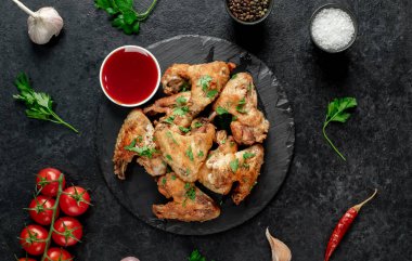 Baharatlı kızarmış tavuk kanatları ve siyah arka planda otlar.