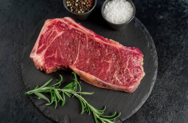 Baharatlı çiğ biftek ve siyah arka planda otlar.