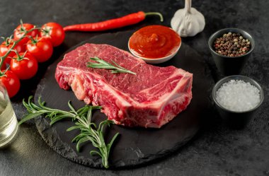 Baharatlı çiğ biftek ve siyah arka planda otlar.