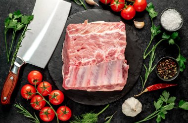 Baharatlı çiğ biftek ve siyah arka planda otlar.