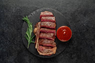 Baharatlı ızgara biftek ve siyah arka planda otlar.