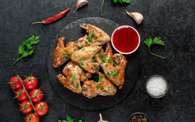 Baharatlı kızarmış tavuk kanatları ve siyah arka planda otlar.