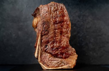 Baharatlı ızgara biftek ve siyah arka planda otlar.