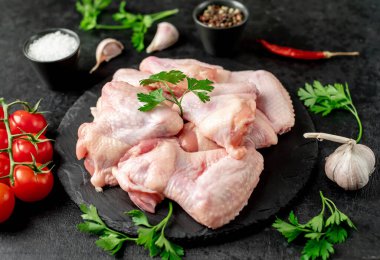 Siyah arka planda baharatlı ve otlu çiğ tavuk kanatları.