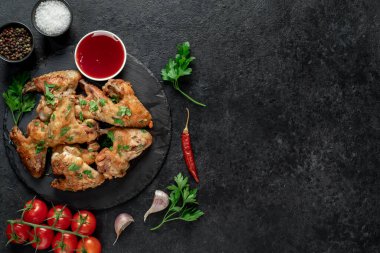 Baharatlı kızarmış tavuk kanatları ve siyah arka planda otlar.