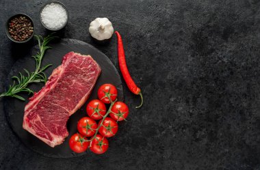 Baharatlı çiğ biftek ve siyah arka planda otlar.