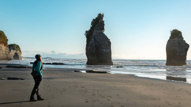 Yeni Plymouth, Yeni Zelanda sahillerinde Üç Kız Kardeş kaya oluşumlarında yürüyen bir kadın. Arkasında Taranaki Dağı 'nı görebilirsin..
