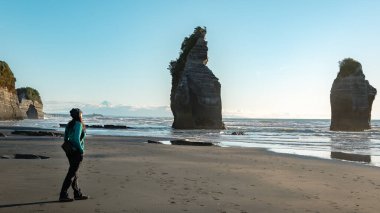 Woman walking in Three Sisters rock formations, coast of New Plymouth, New Zealand. You can see Mount Taranaki behind. clipart
