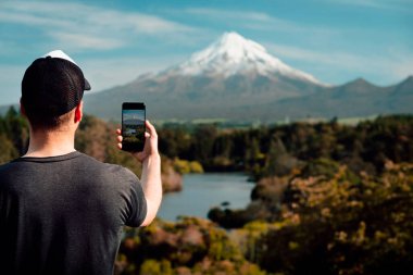 Yeni Zelanda 'daki Taranaki Dağı' nda cep telefonuyla fotoğraf çeken adam. Kaydırmayı kopyala
