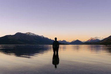 Wakatipu Gölü 'nün içindeki adam karlı dağ tepelerinin arkasındaki inanılmaz günbatımını seyrediyor. Yeni Zelanda manzarası