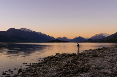 Man fishing on Lake Wakatipu at sunset with the amazing view of mountains behind. Otago, New Zealand.