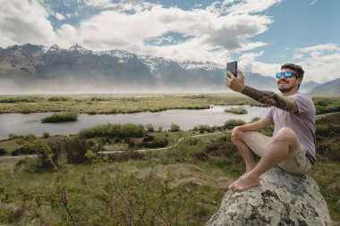 Glenorchy 'de cep telefonuyla güzel dağ manzaralı bir selfie çeken bir adam. Yeni Zelanda manzarası.